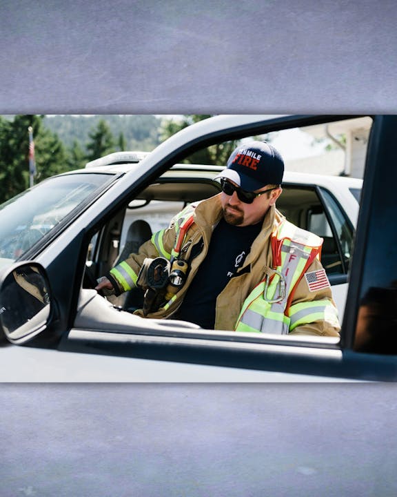 A firefighter in gear, seen through a car window.
