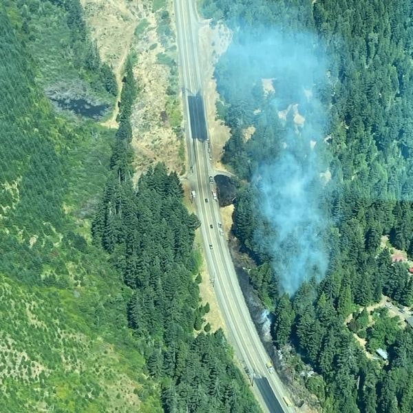 Aerial view of a highway with smoke rising from a forest area.