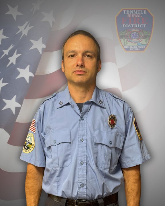 A uniformed firefighter with US flag background and fire district emblem.