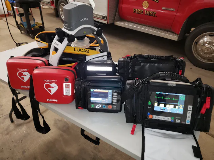 The image shows medical equipment, including defibrillators and monitors, commonly used in emergency medical services.
