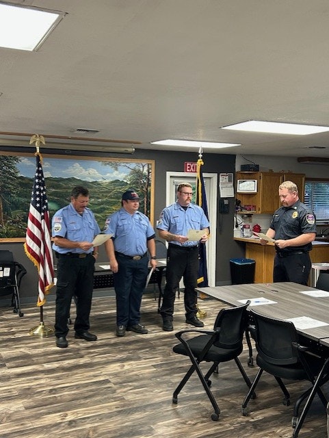 A group of four men, including uniformed officers, are gathered in a room for what appears to be a ceremony or presentation.