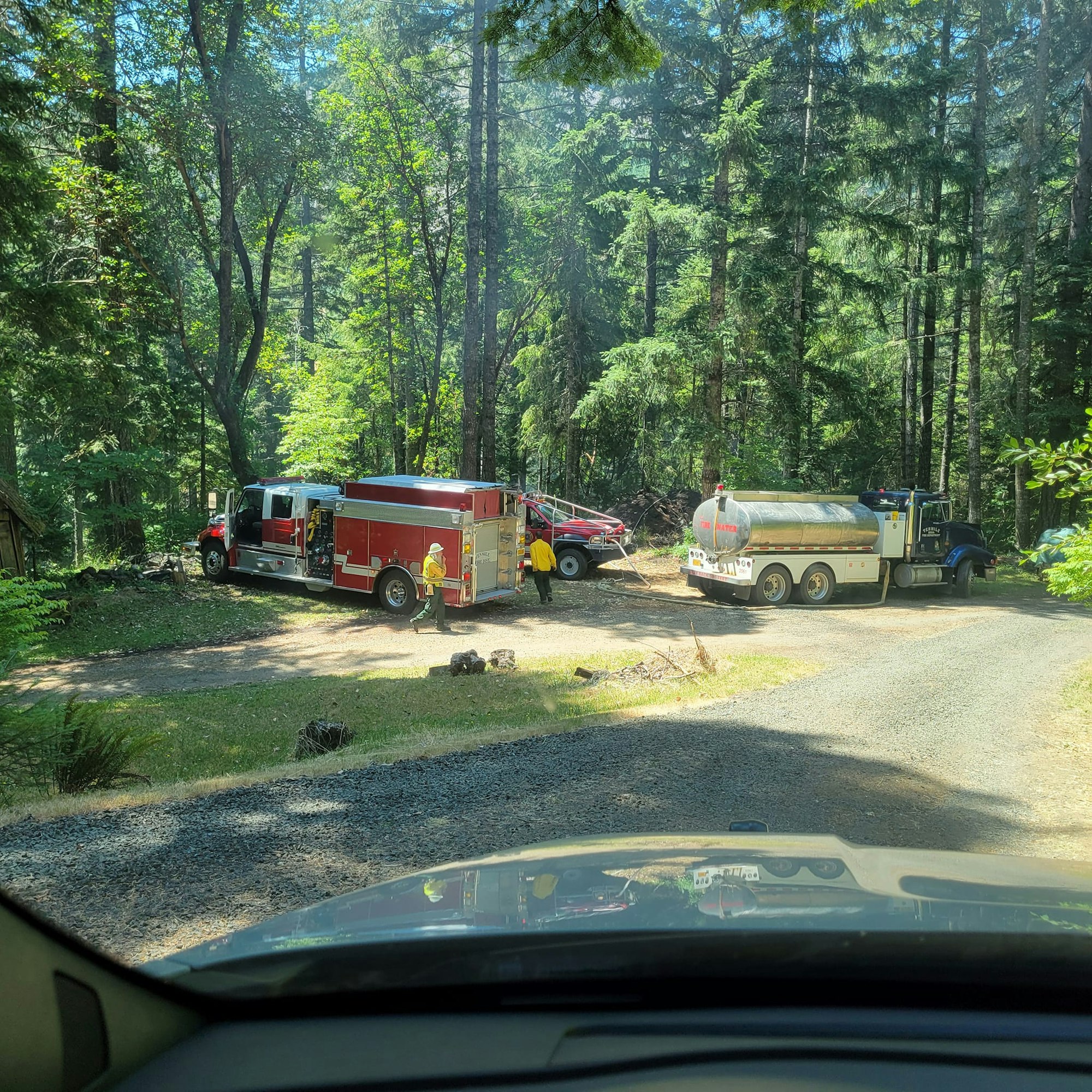 A fire engine, a water tanker, and firefighters in a wooded area, likely responding to an emergency.