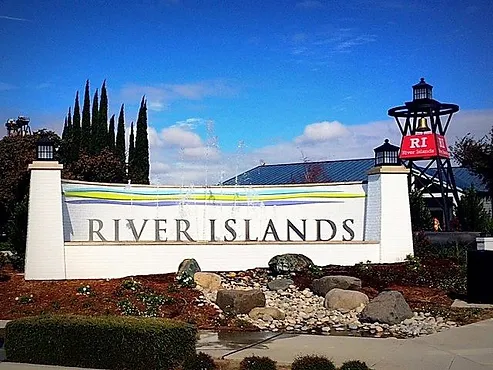 A sign that says "RIVER ISLANDS" with rocks and plants in front, and a lighthouse structure in the background under a blue sky.