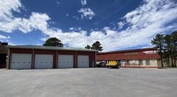 A brick building with multiple garage doors and a parked emergency vehicle under a partly cloudy sky.