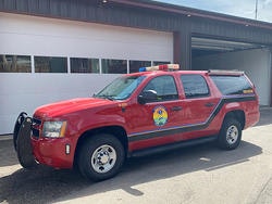 A red emergency vehicle with a roof light bar, parked in front of a garage.