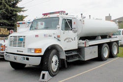 White tanker truck parked on a street with some text on the cab and tank.