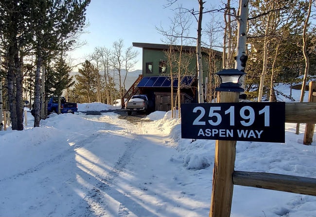 Snowy driveway leading to a modern house, surrounded by trees, with a sign reading "25191 Aspen Way."