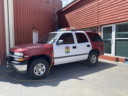 A red and white emergency vehicle parked beside a building, with a hose attached.