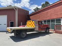 A red fire truck with a flatbed parked outside a red building on a sunny day.