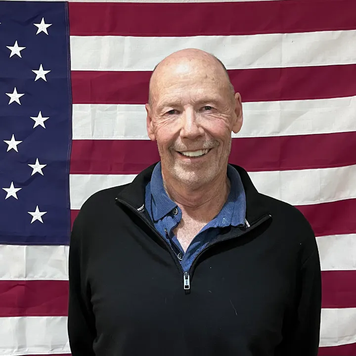 A man smiling in front of an American flag.