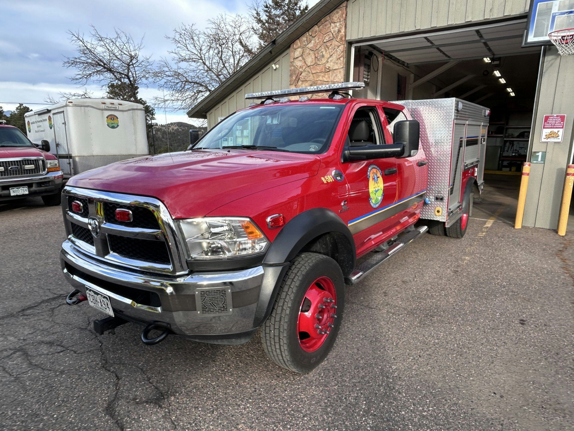 A red fire truck with a utility bed is parked outside a building, showing its emergency lights and equipment.