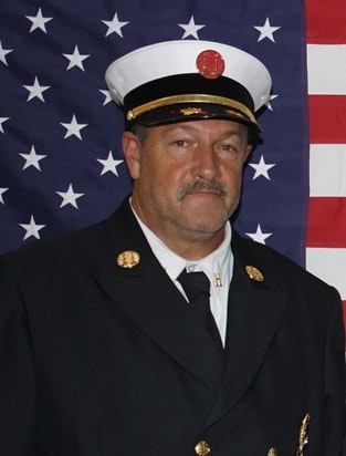 The image features a person in a formal uniform with a hat, standing in front of an American flag.