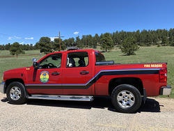A red fire rescue pickup truck parked on a rural road with trees in the background.