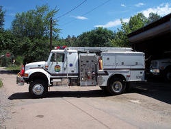 A fire truck is parked outside a building with trees and a clear sky in the background.