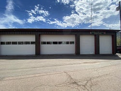 A building with three large garage doors under a blue sky with clouds.