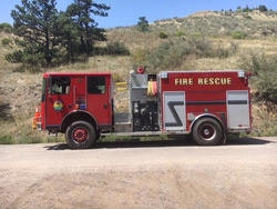 A red fire rescue truck parked on a dirt road with a hillside background.