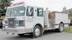 A white fire truck with equipment on the side, parked outdoors.