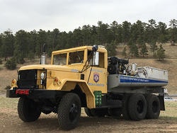 A yellow fire truck parked on a grassy area, surrounded by trees.