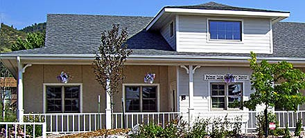 A suburban house with a gabled roof, white fence, and shrubs, under a clear sky.