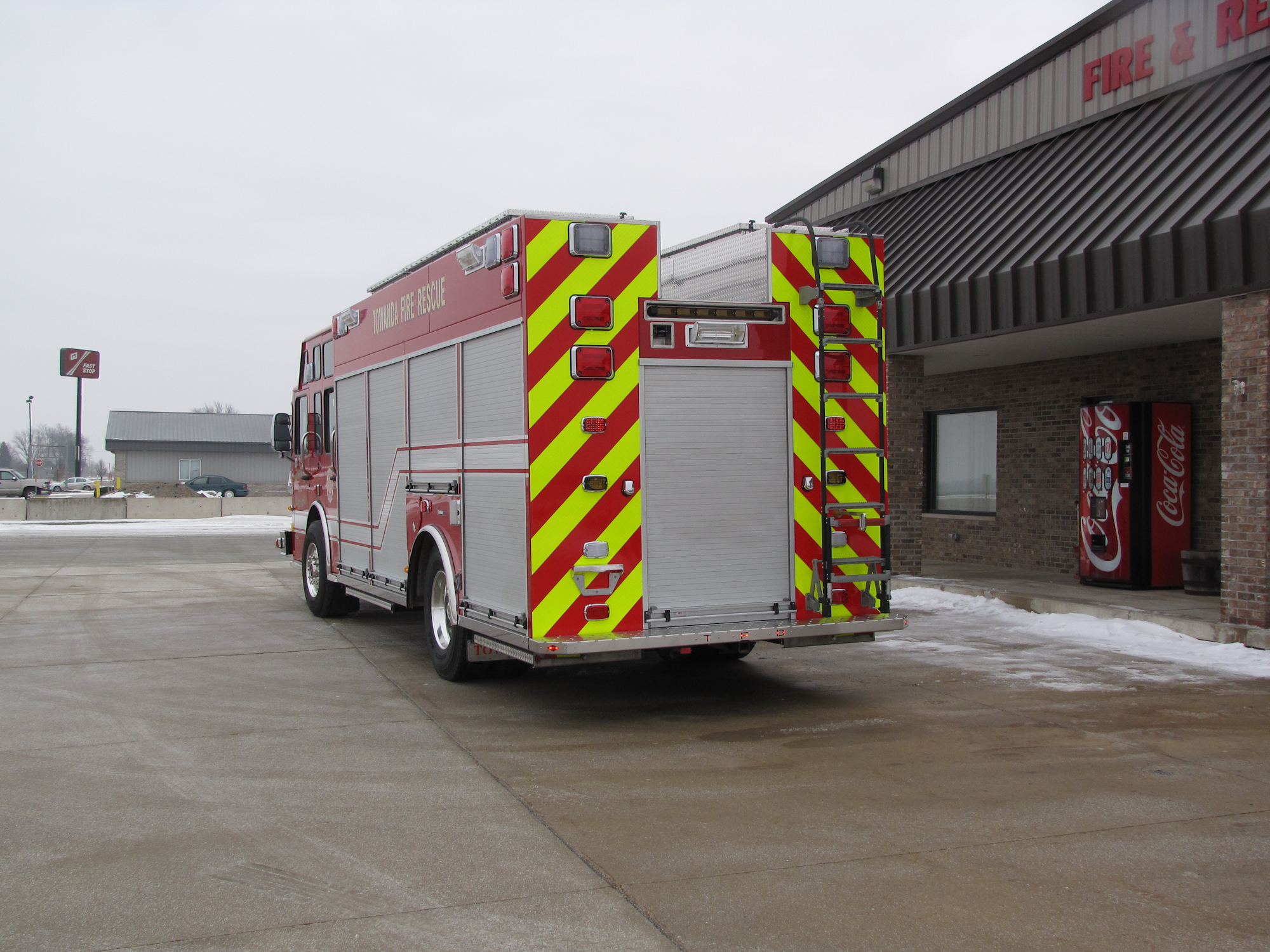 Red fire truck parked outside a fire station near a vending machine and snow-covered ground.