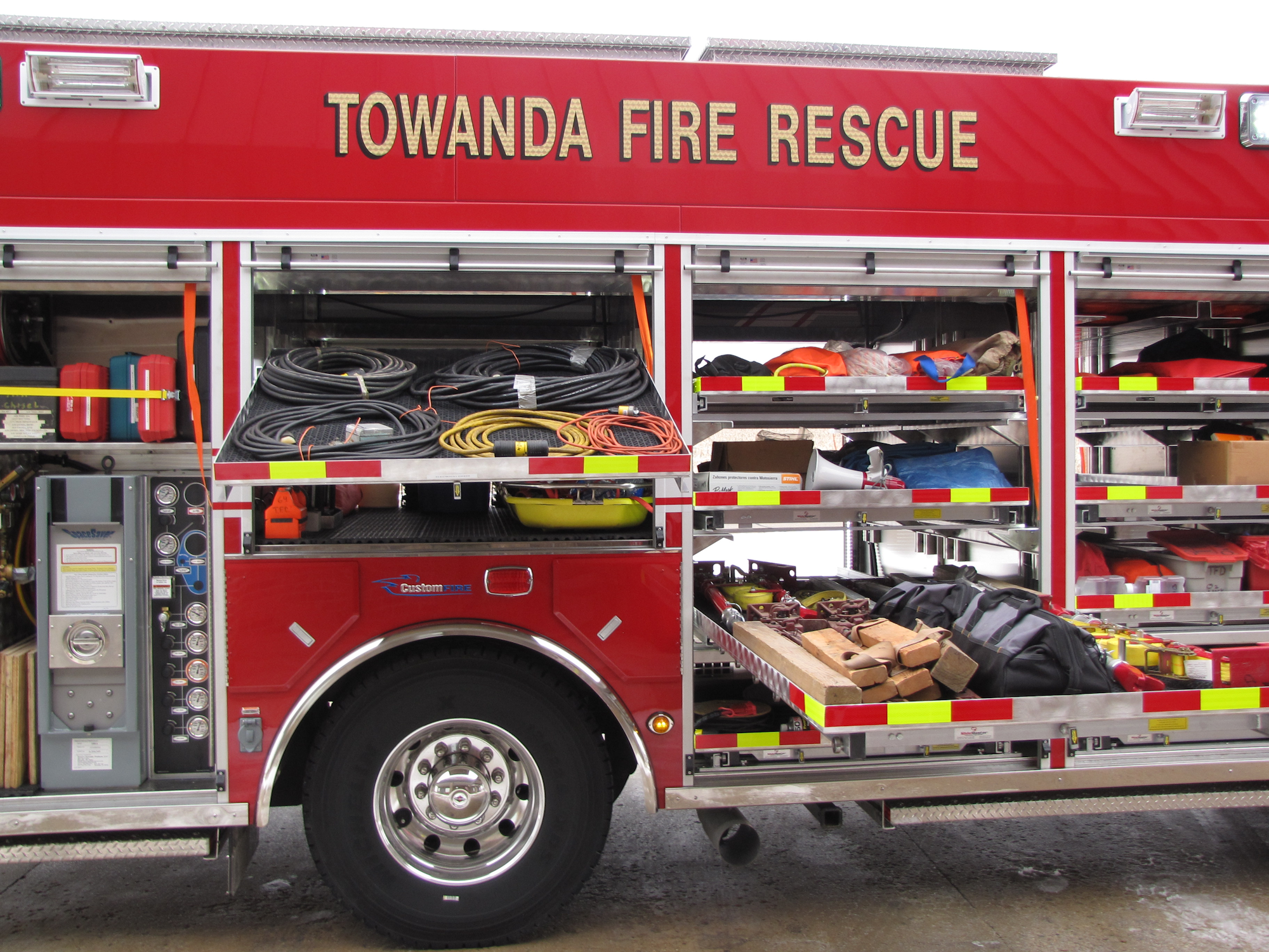 Fire rescue truck with open compartments showing hoses, tools, and equipment.