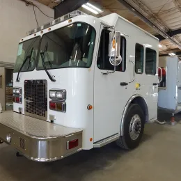 A white fire truck parked indoors, with a boxy design and large windows.