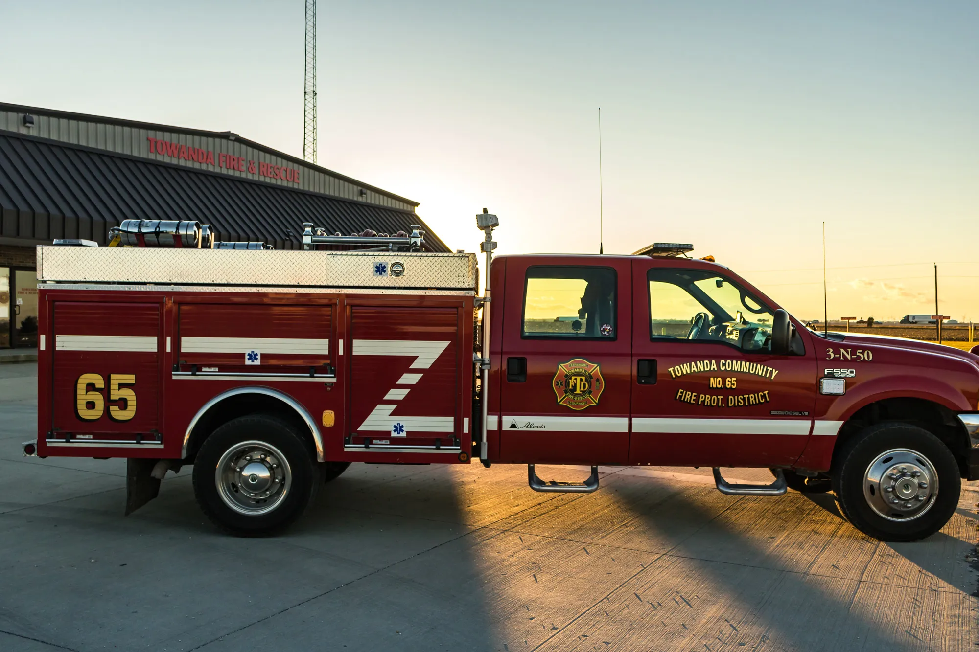 A red fire rescue truck parked outside a fire station at sunset.