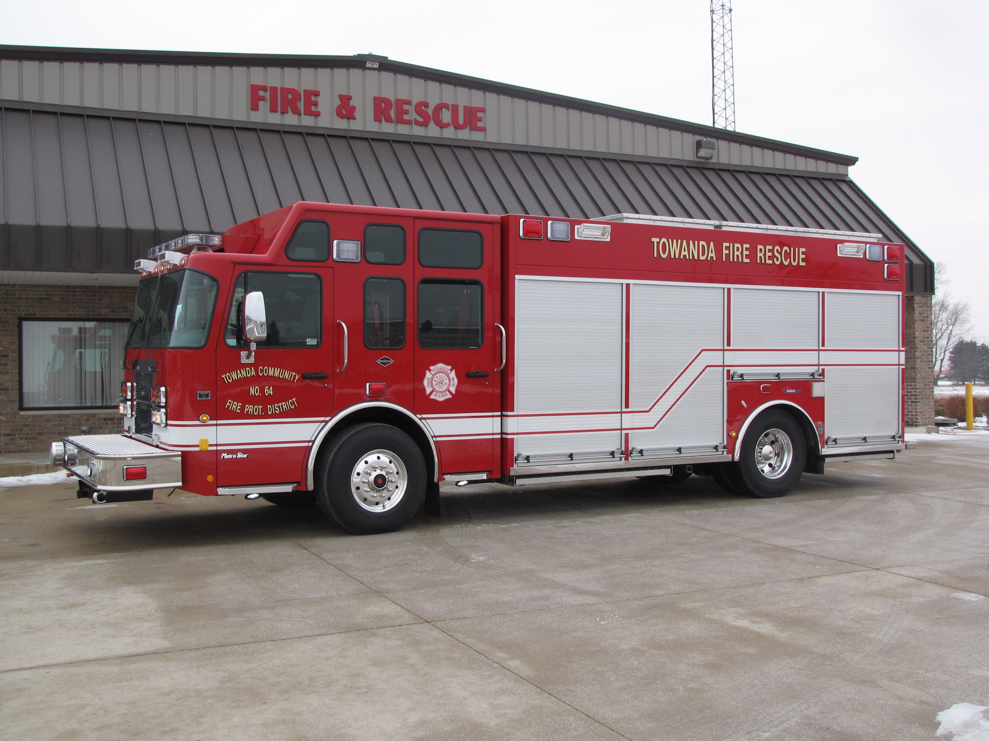 A red fire rescue truck parked in front of a fire station labeled "FIRE & RESCUE."