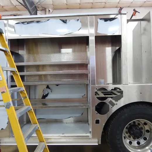 A partially assembled or repaired truck with open compartments and a ladder beside it.