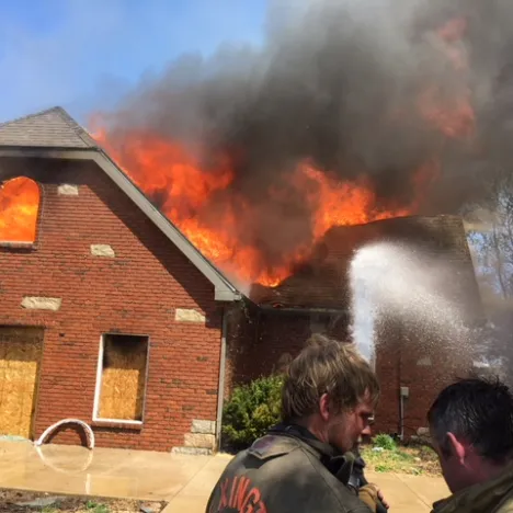 Firefighters combating a large fire in a house with intense flames and heavy smoke.