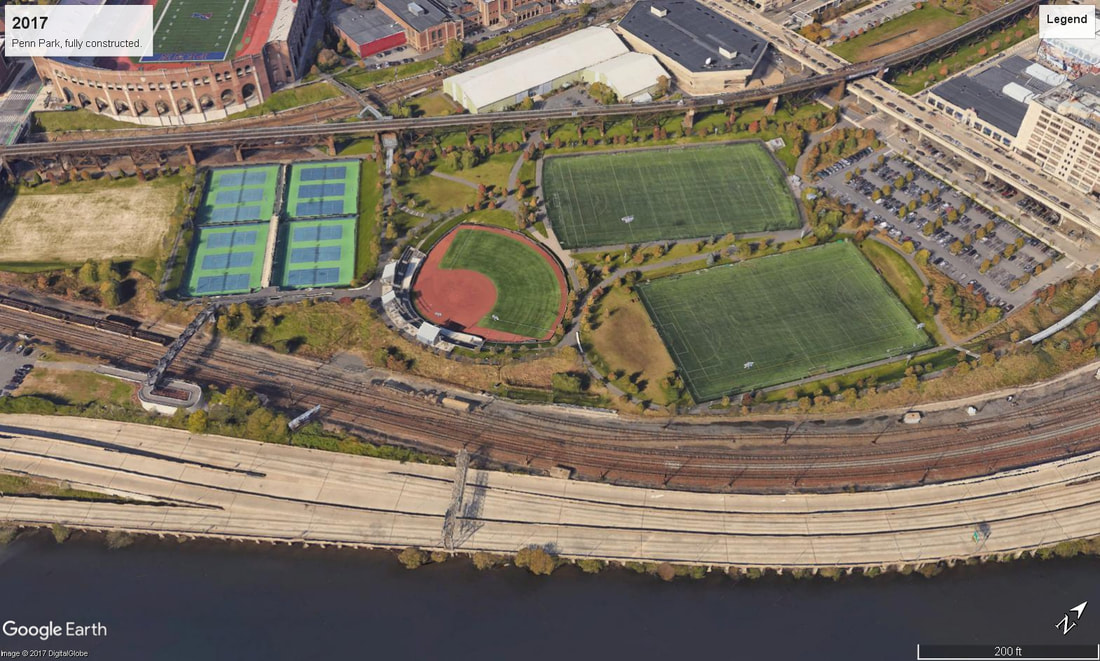 Aerial view of a park with sports fields, tennis courts, a running track, train tracks, a river, and roads.