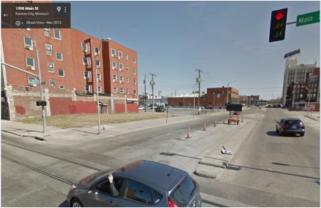 Urban street view with cars, traffic lights, and buildings under a clear sky. There's also a Google Street View watermark.