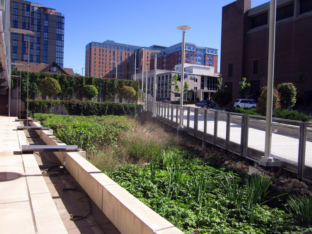Urban park with seating, fencing, greenery, and surrounding buildings under a clear sky.