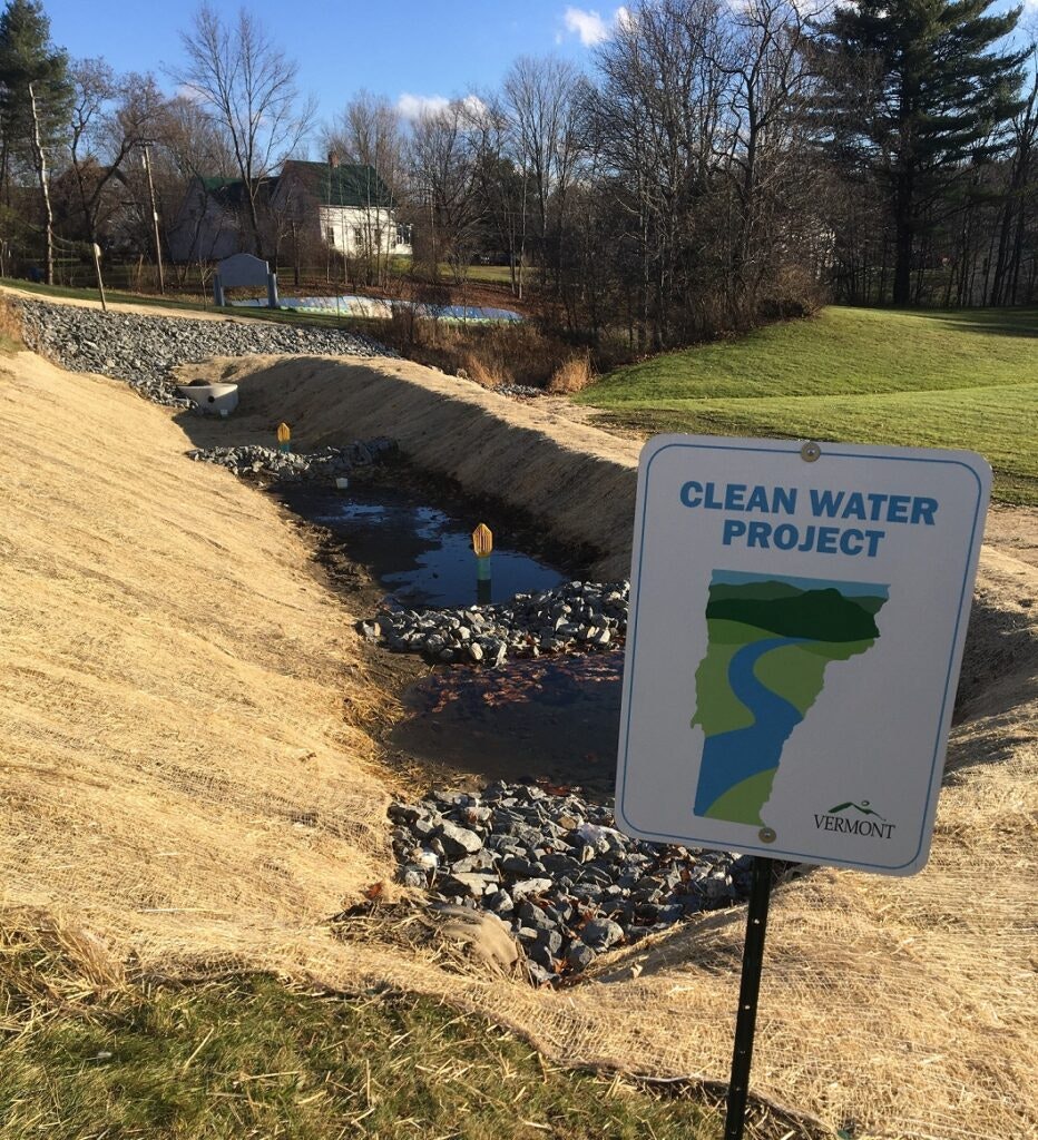 A ditch with water and a sign reading "CLEAN WATER PROJECT" by Vermont.