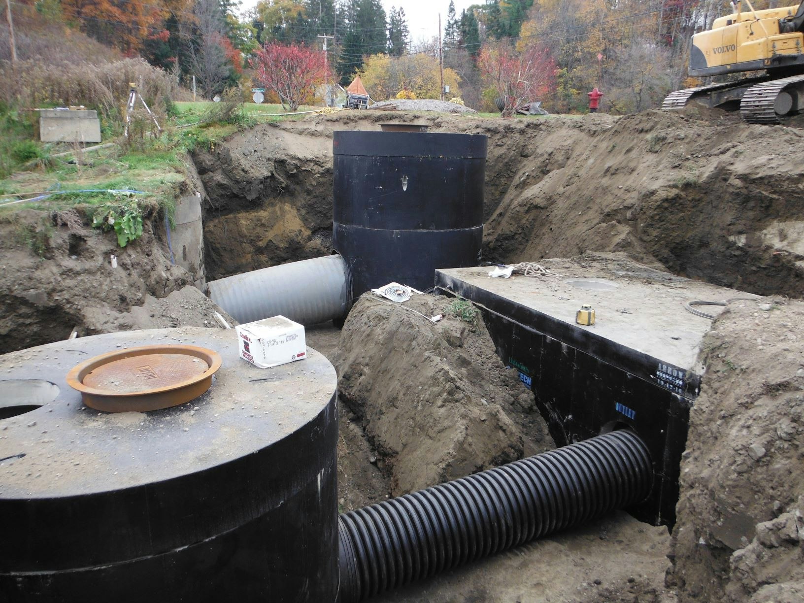 Excavation site with large pipes and tanks being installed, surrounded by dirt and construction equipment.