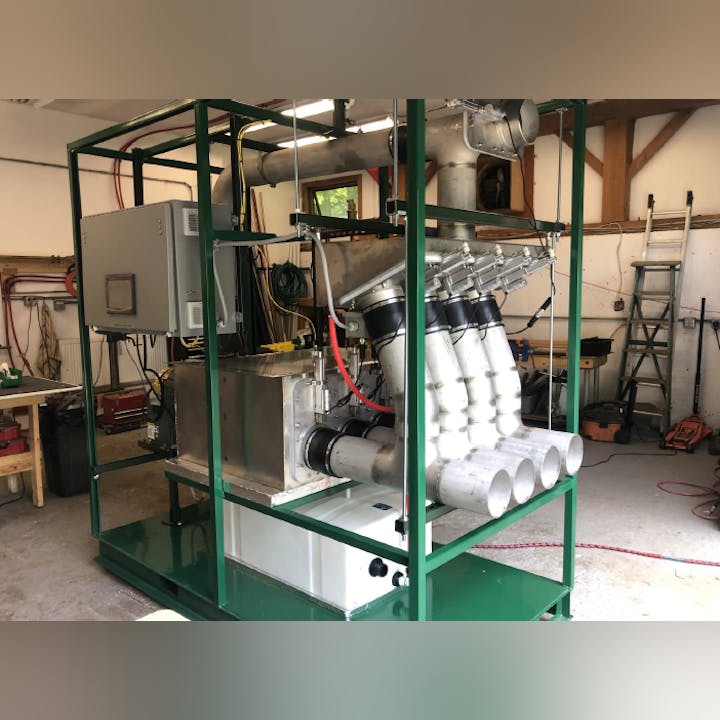 A green-framed mechanical setup with pipes, connectors, and a control box in a workshop setting.