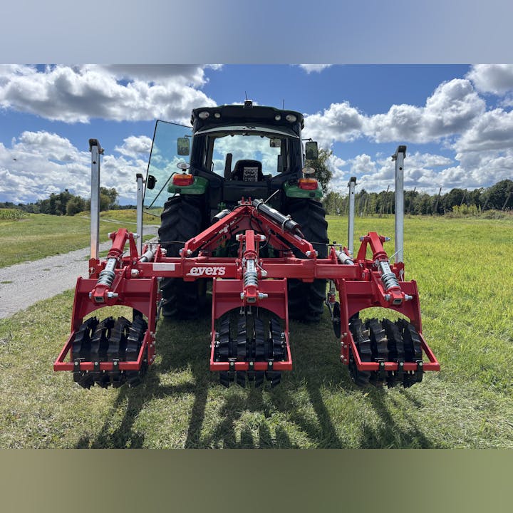A red subsoiler attached to a tractor in a field under a partly cloudy sky.