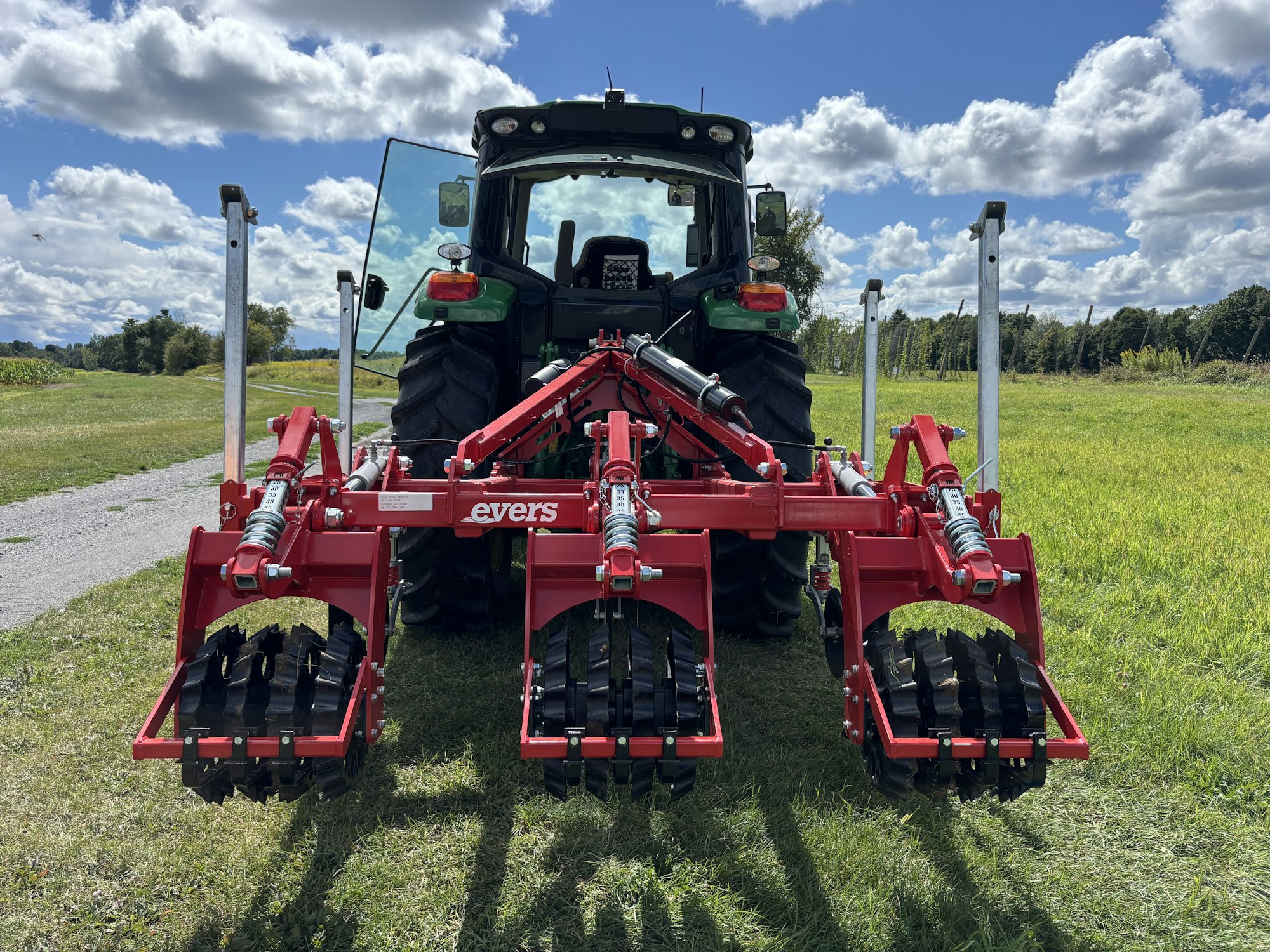 A red subsoiler attached to a tractor in a field under a partly cloudy sky.