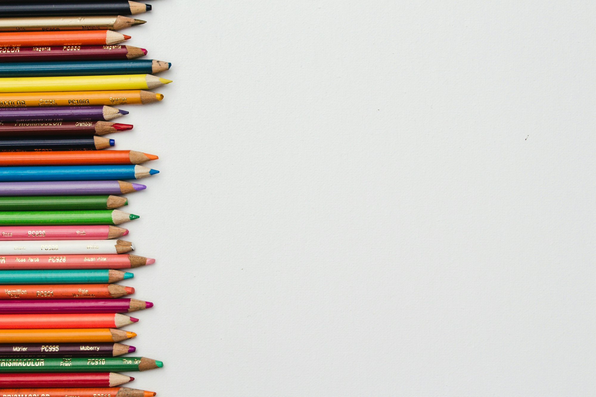 Colored pencils arranged in a vertical line on the left side, against a blank white background.