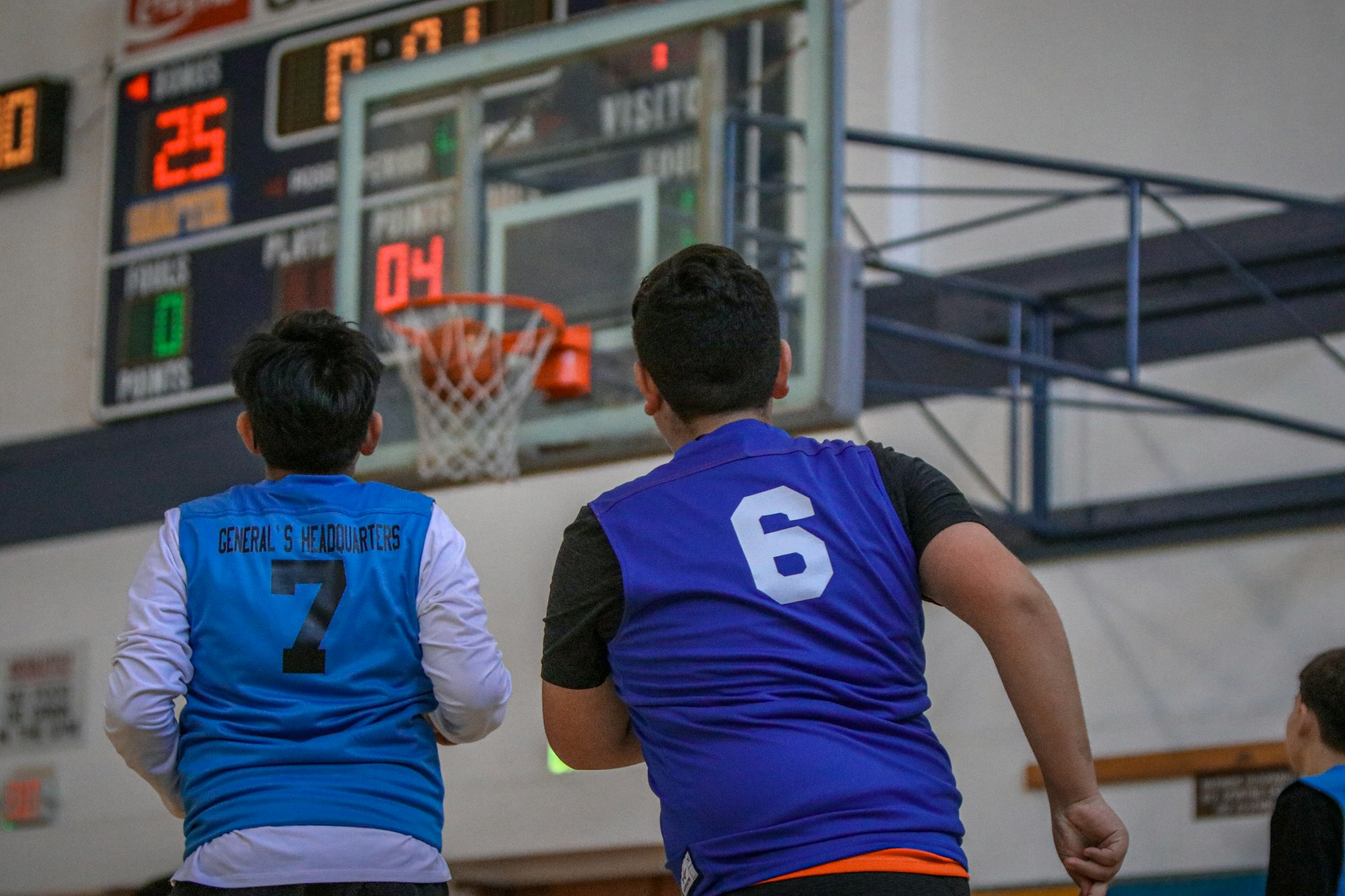 Two basketball players watch the shot clock, jerseys numbered 6 and 7, with the scoreboard in the background.