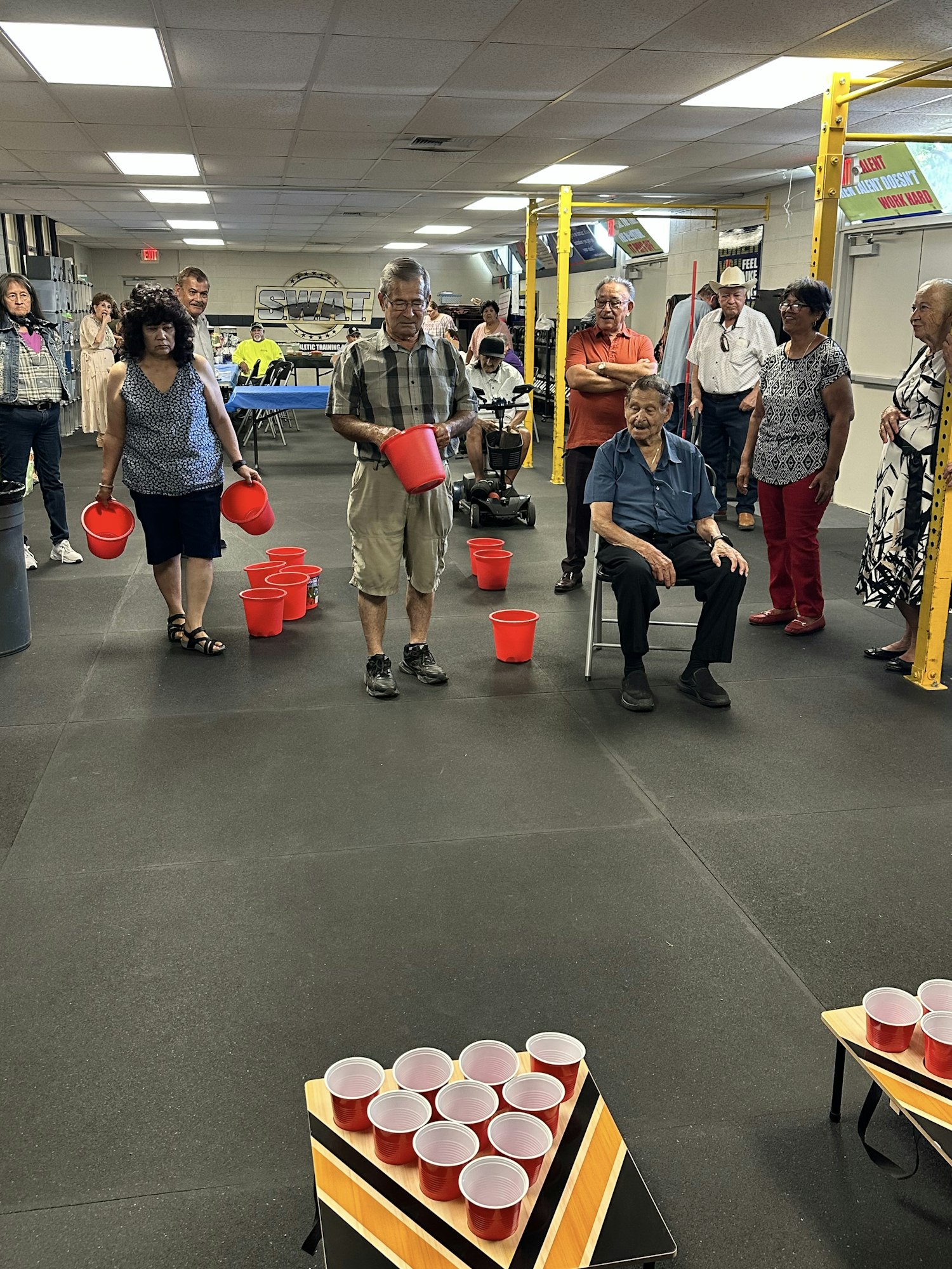 People in a room with red buckets and tables set up with red cups, possibly playing a game.