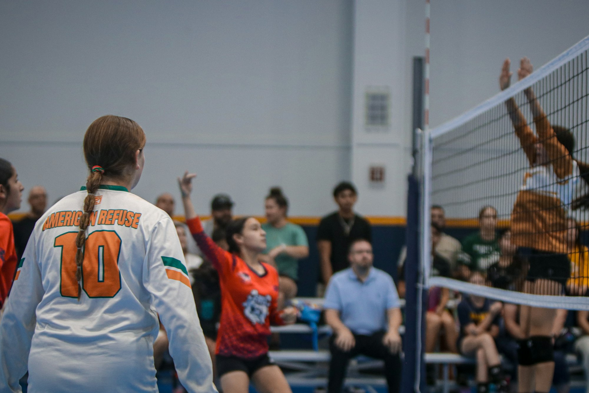 A volleyball match in action with players, a referee, and spectators.