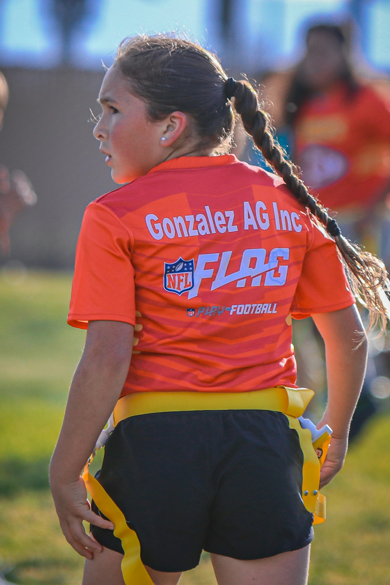 A girl wearing an NFL FLAG shirt with "Gonzalez AG Inc" on the back, playing flag football.