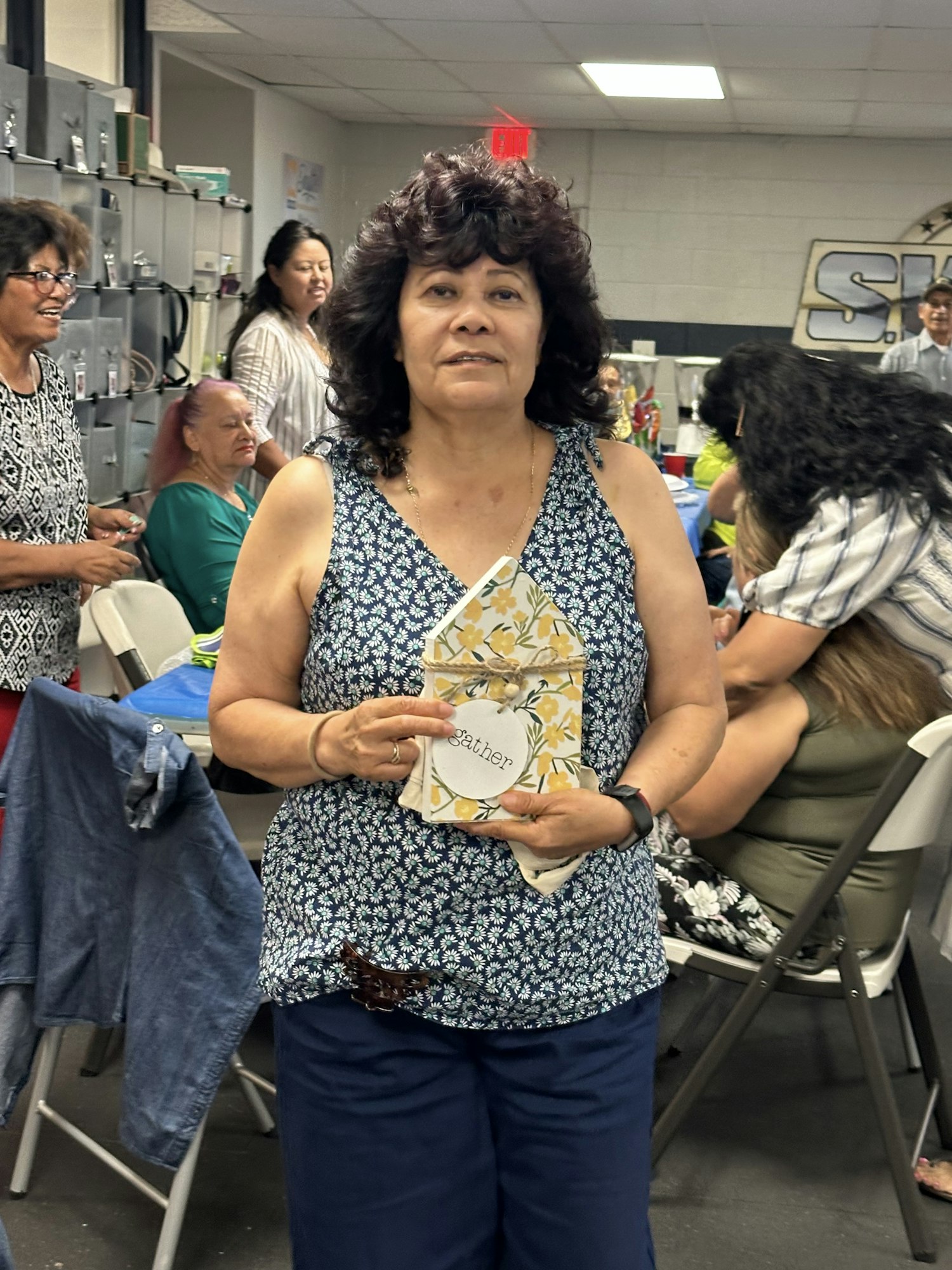 A woman holds a "gather" sign, surrounded by people seated in a room.