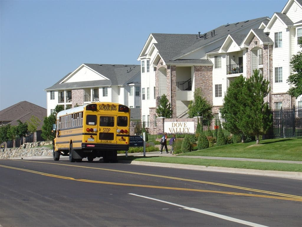 Yellow school bus parked on a street near apartments labeled "Dove Valley".