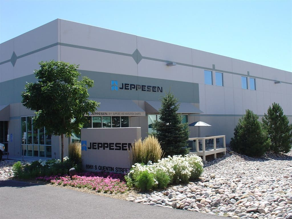 A building with "Jeppesen" signage, surrounded by plants and a pathway, in a sunny setting.