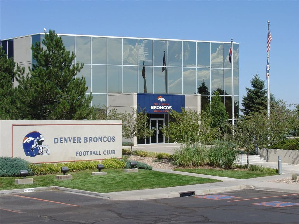 Denver Broncos Football Club building with reflective windows, sign, and flags outside.