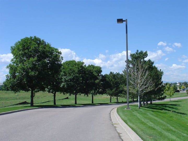 A curved road lined with trees and a streetlamp under a bright blue sky with scattered clouds.