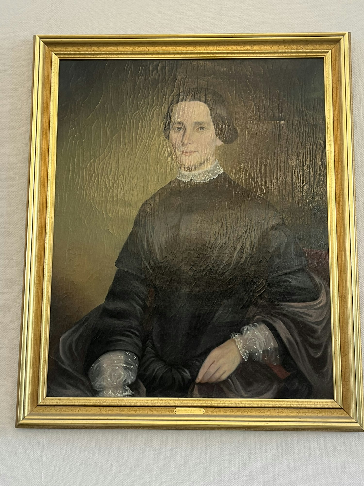 A portrait of a woman in a dark dress with a lace collar in a gold frame, displayed on a wall.
