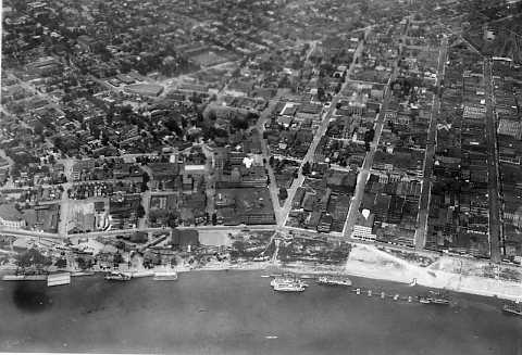 Aerial view of a coastline city with buildings, streets, and docks with ships. Vintage black and white photo.